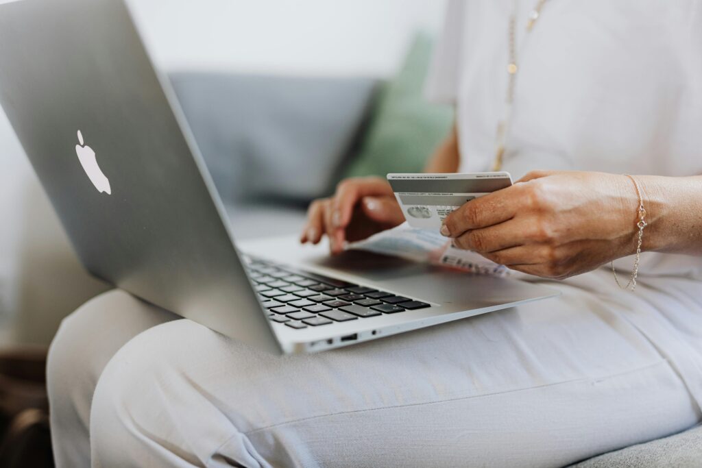 Close-up of a person holding a credit card while shopping online using a laptop at home.